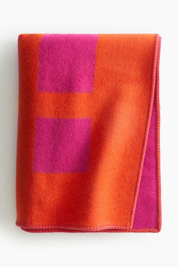 an orange and pink blanket on top of a white surface with a red square in the middle