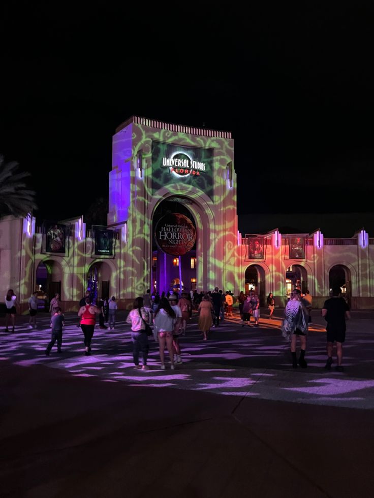 people are walking around in front of a building with projected lights on it at night