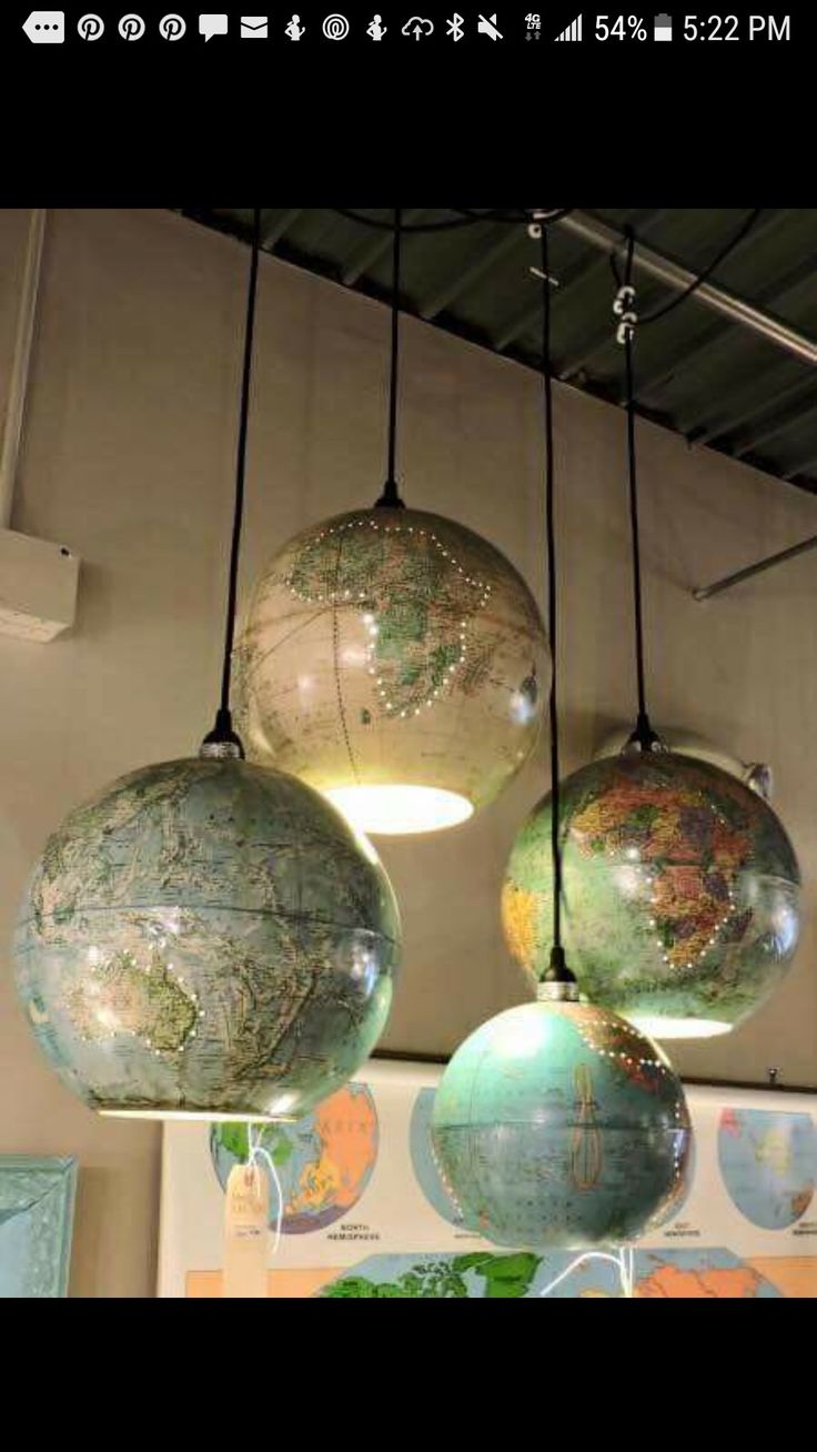 three globes hanging from the ceiling in a room with maps on it and lights above them