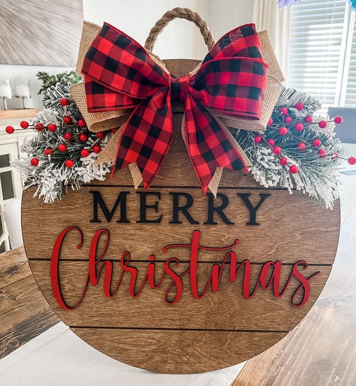 a wooden sign that says merry christmas with red and black plaid bows on it's front