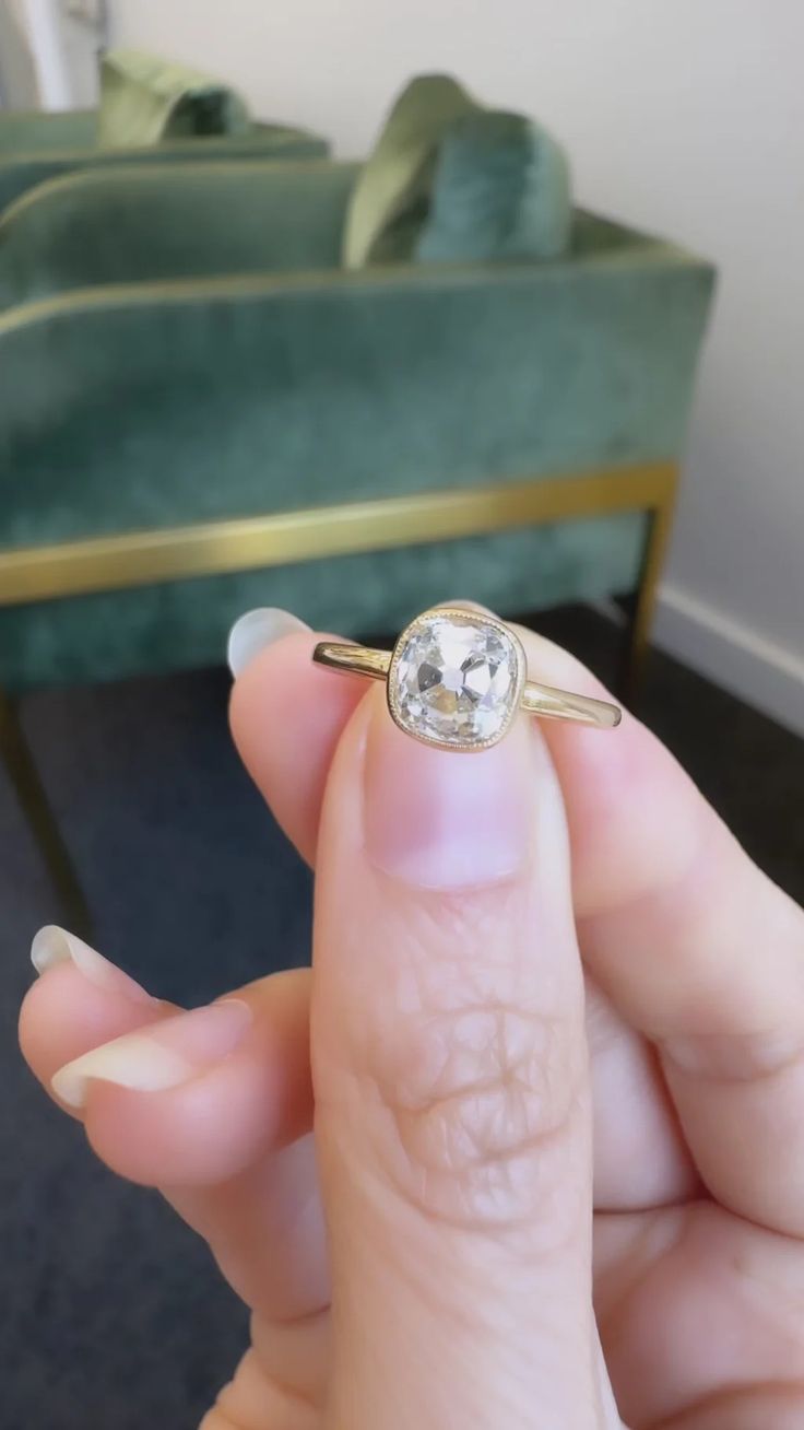 a woman's hand holding an engagement ring in front of a green velvet couch