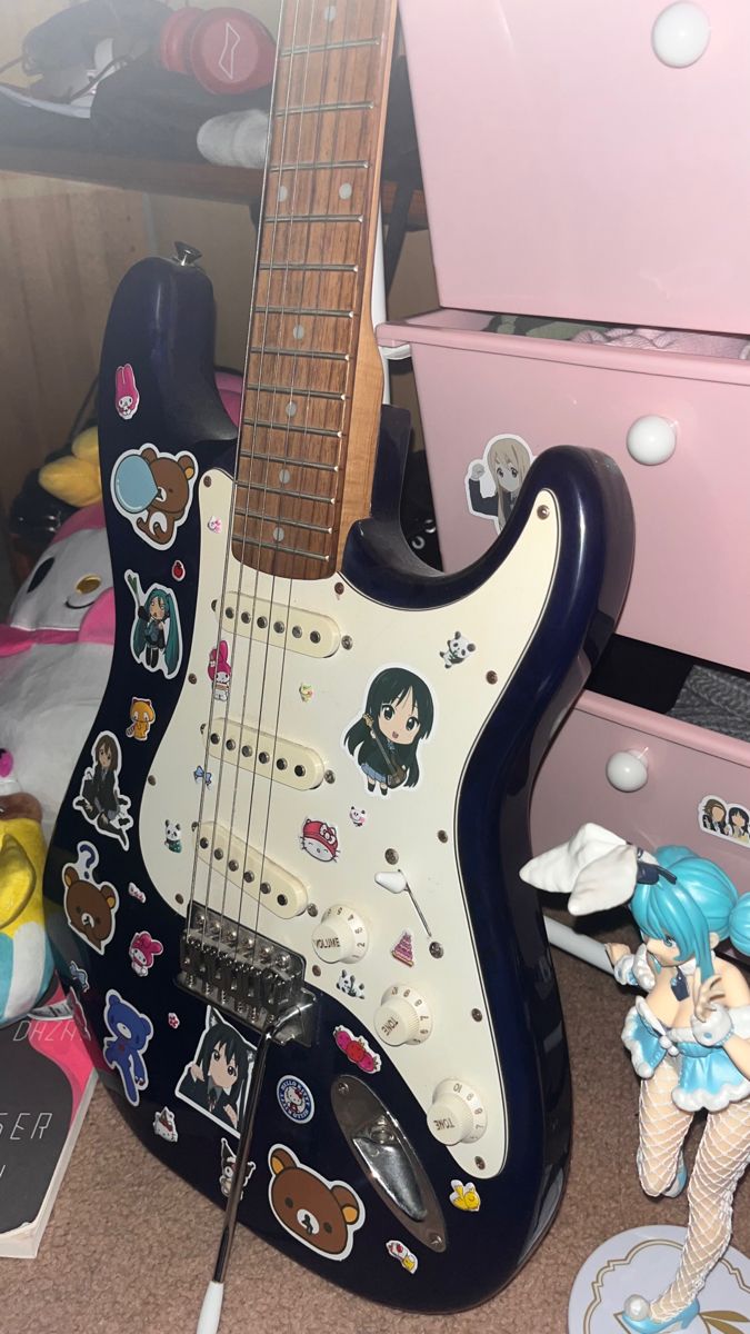 an electric guitar with many stickers on it's body and neck, sitting next to other toys