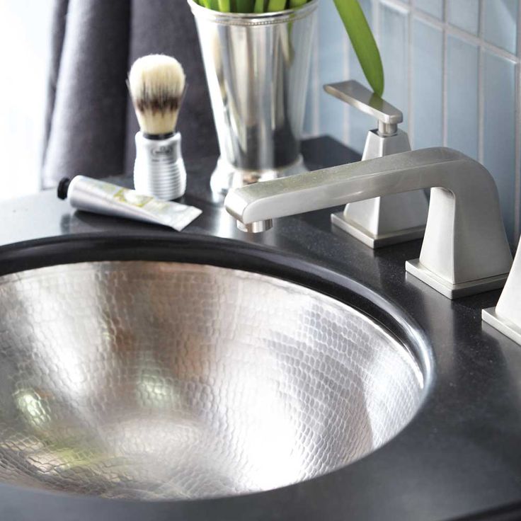 a close up of a bathroom sink with a toothbrush and flowers in a vase