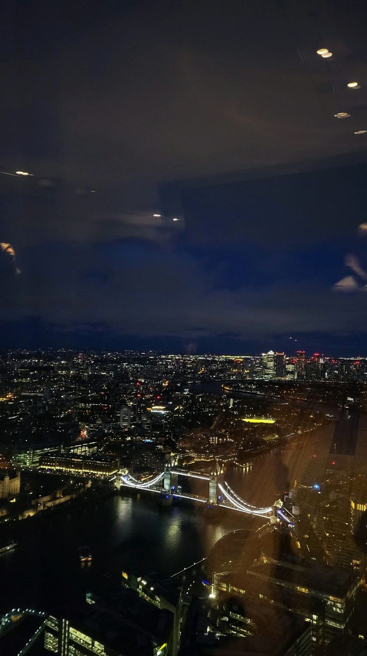 an aerial view of the london skyline at night with lights in the sky and water below