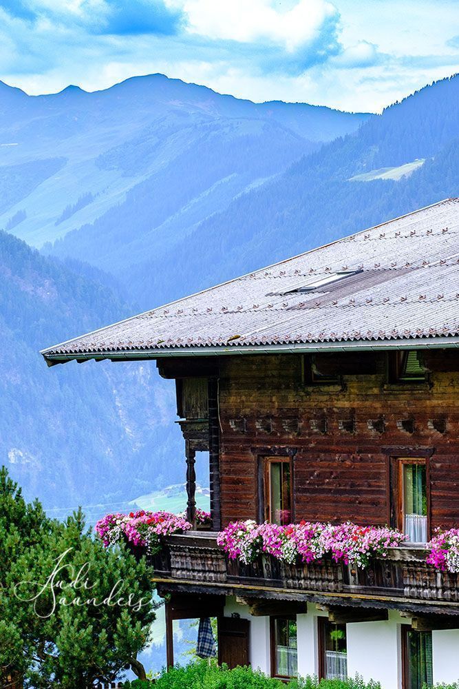 a house with flowers on the balcony and mountains in the background