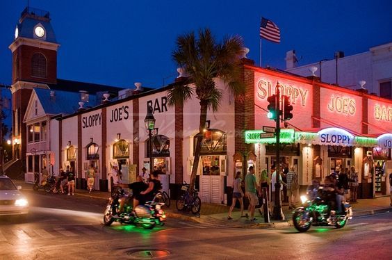 two motorcycles are parked on the street in front of a building with neon lights and palm trees