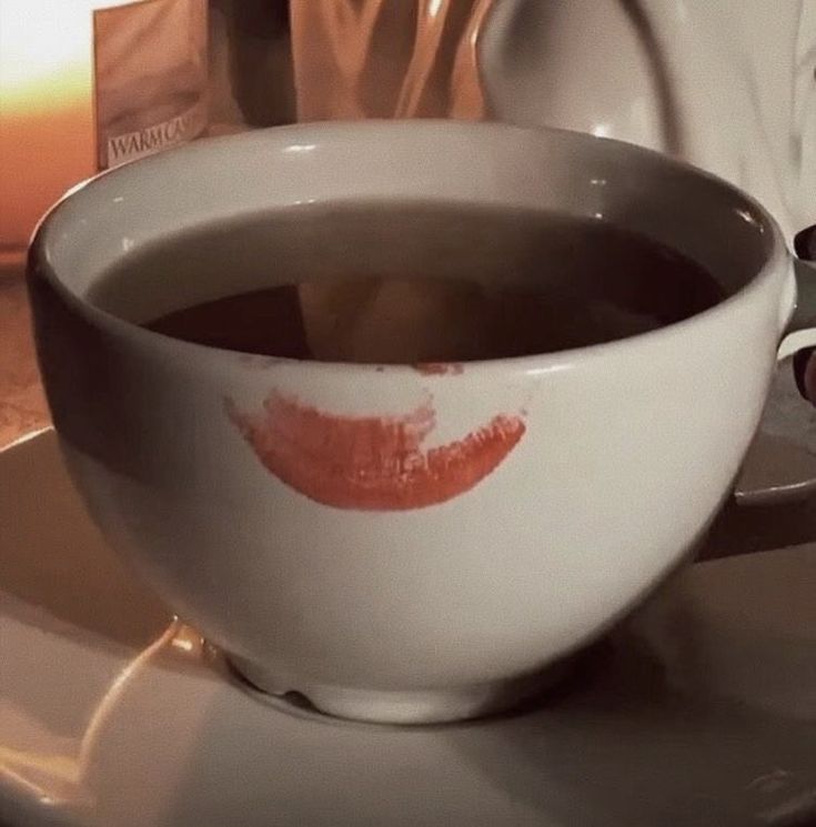 a white cup with red lipstick on it sitting on a saucer next to a plate