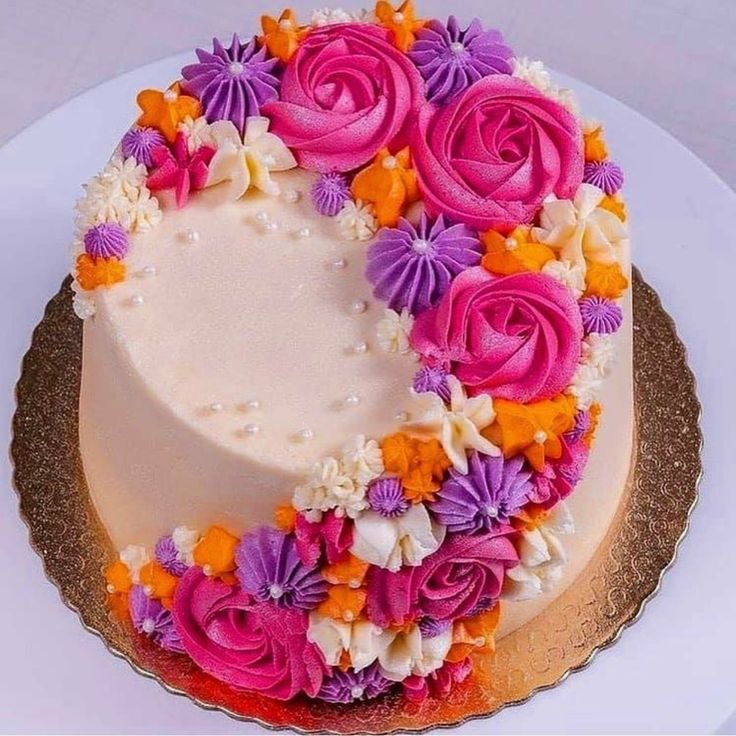 a white cake with pink and purple flowers on it's top is sitting on a gold plate