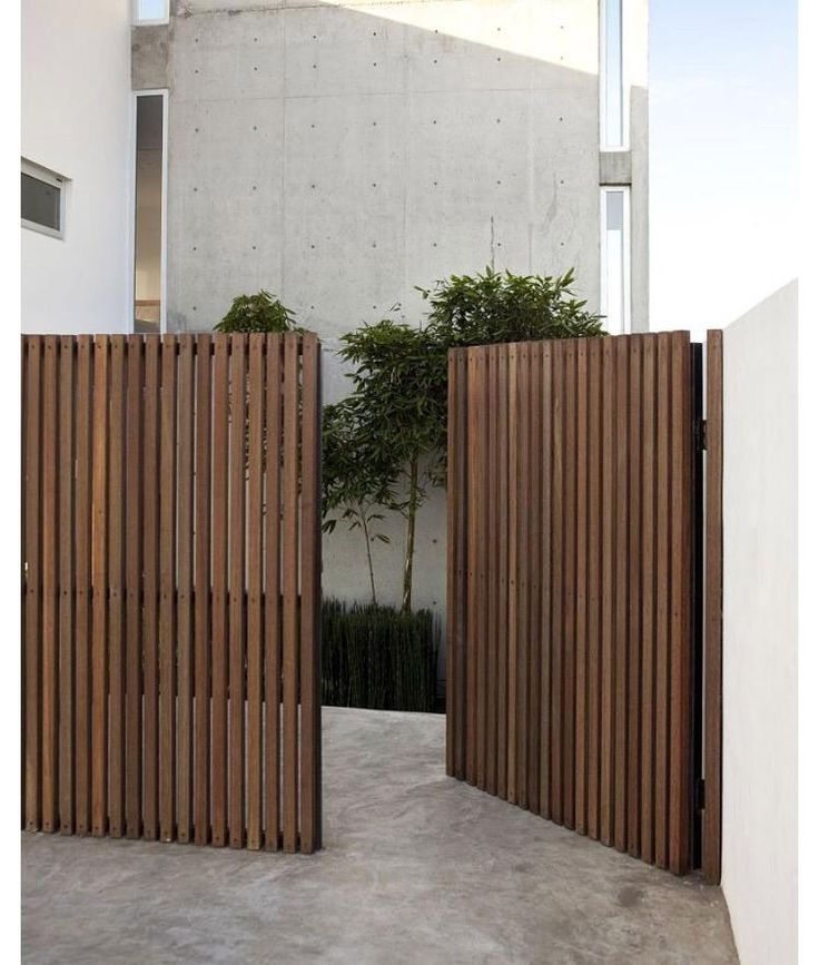 two wooden gates are open in front of a white building with a tree on the other side