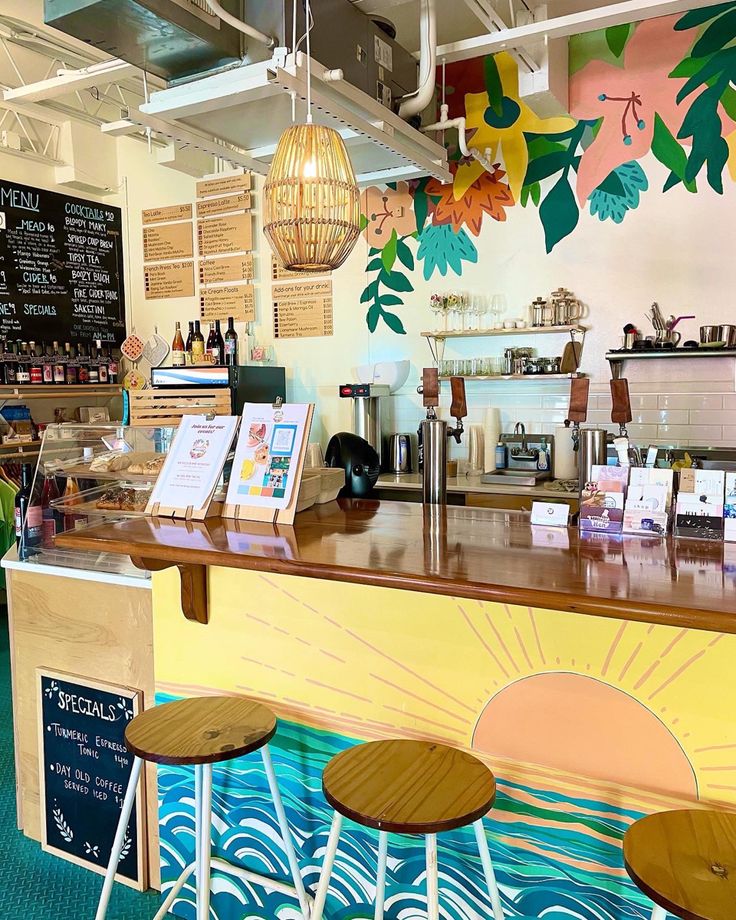 the inside of a coffee shop with colorful murals on the wall and wooden stools