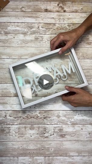 two hands are holding a framed sign with the words dream written on it and another hand is pointing at it