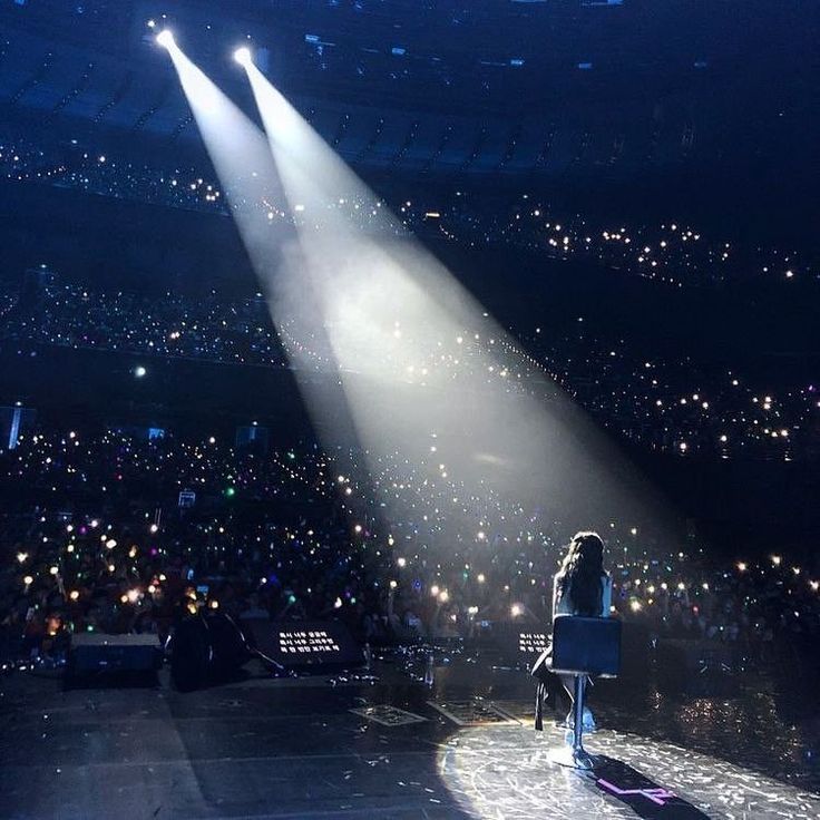 a woman standing on top of a stage under two spotlights in front of a crowd