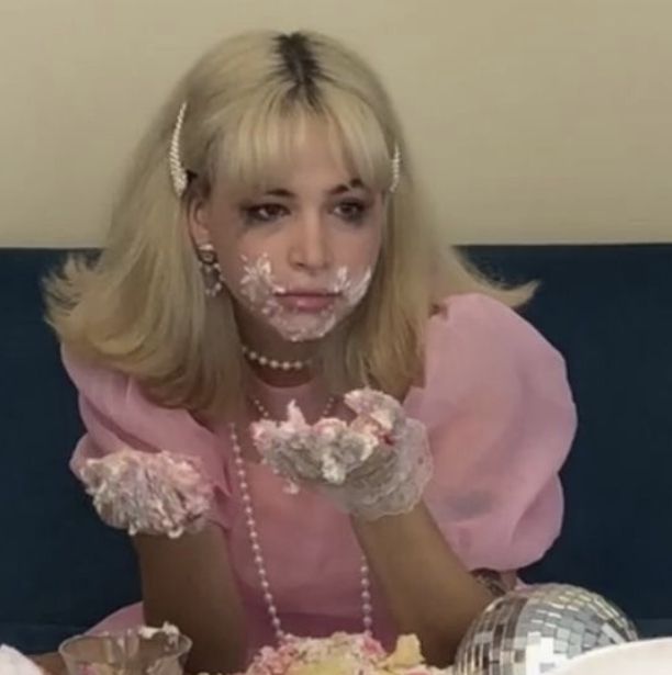 a woman in pink is sitting at a table with cake and confetti on her face