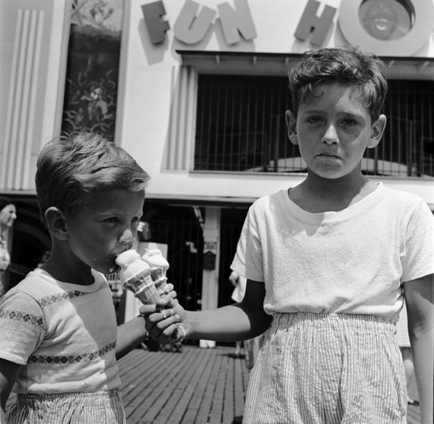 two young boys standing next to each other while eating ice cream in front of a building