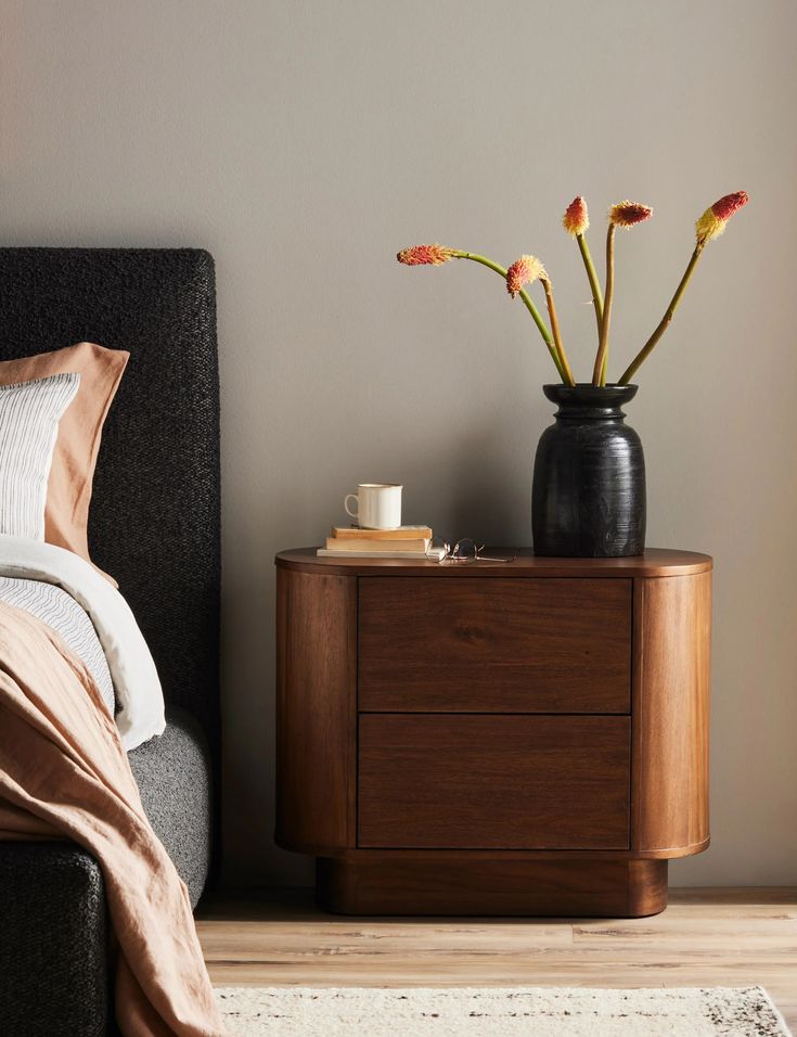 a bedroom with a bed, nightstand and flowers in a vase on the end table