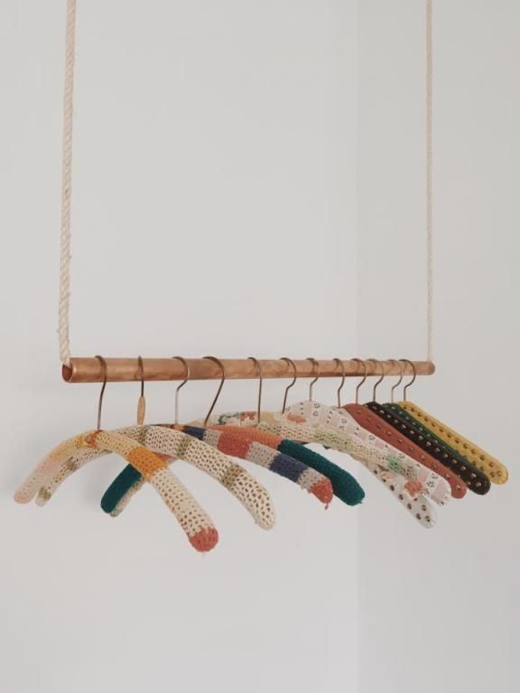 an assortment of knitted gloves hanging from a wooden hanger on a white wall