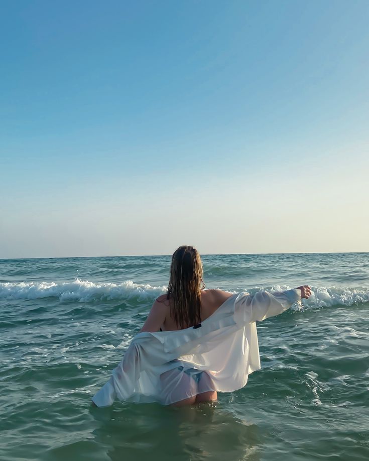 a woman sitting in the ocean with her arms spread out and looking at the water