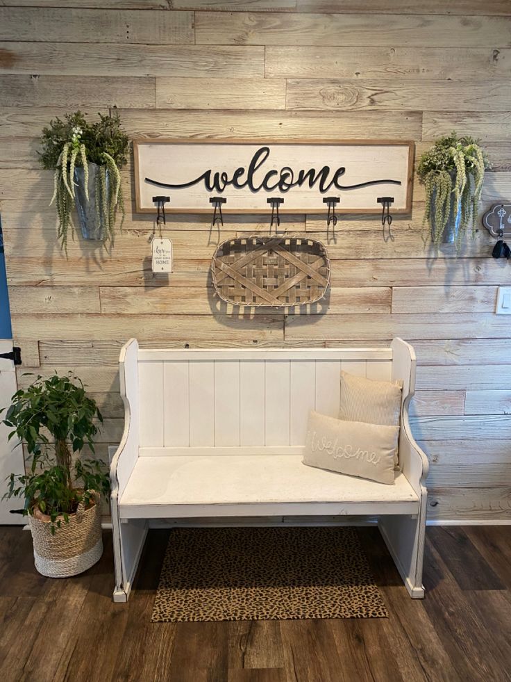 a white bench sitting in front of a welcome sign and potted plants on the wall