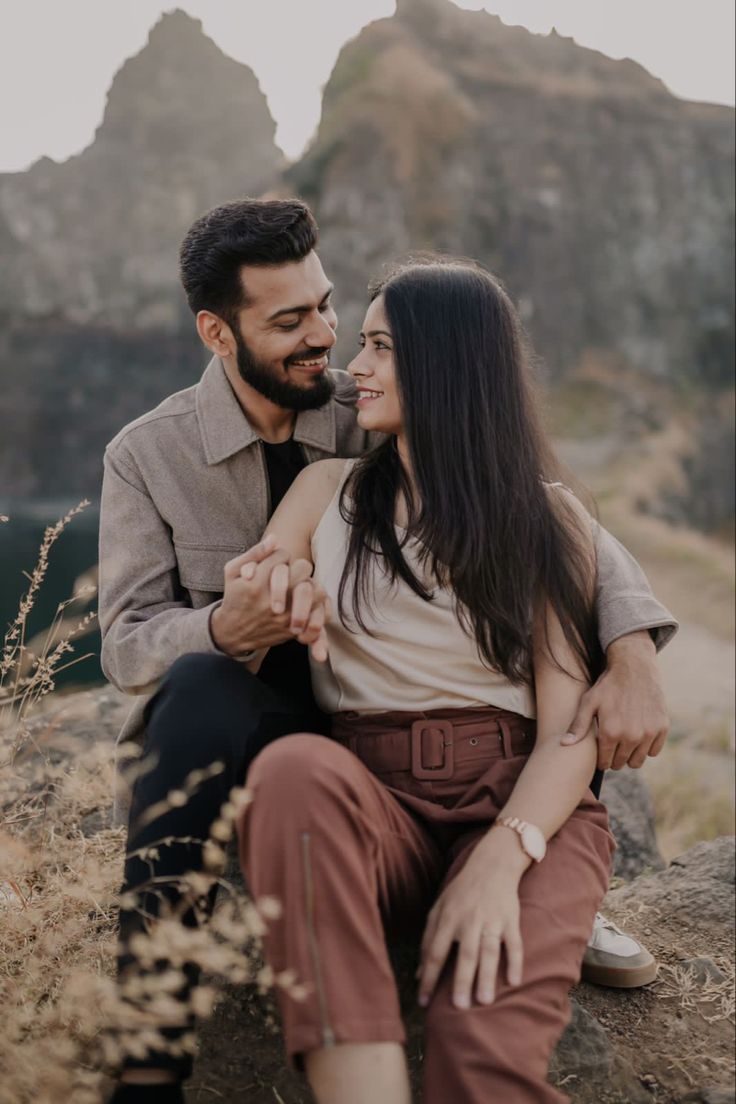 a man and woman sitting on top of a rock