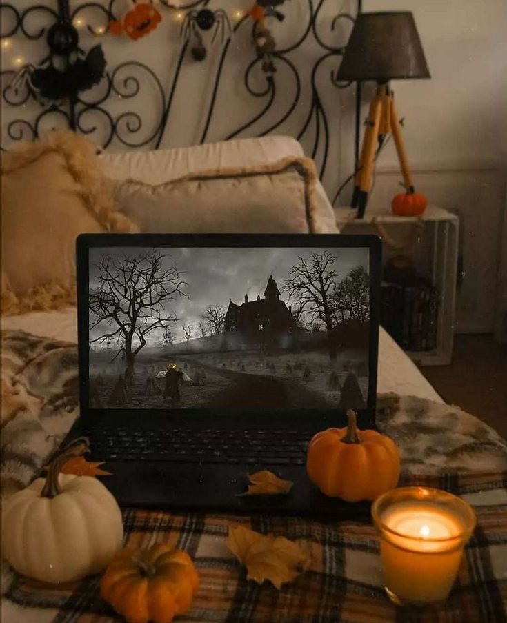 an open laptop computer sitting on top of a bed next to candles and pumpkins