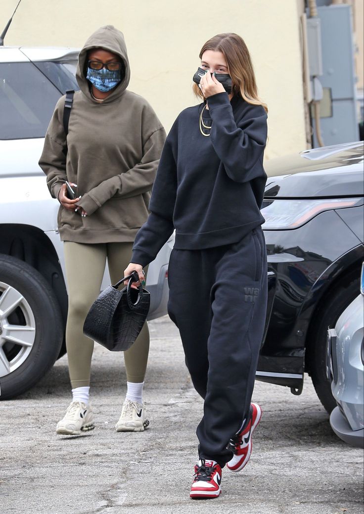 two women walking down the street while wearing face masks and holding cell phones in their hands