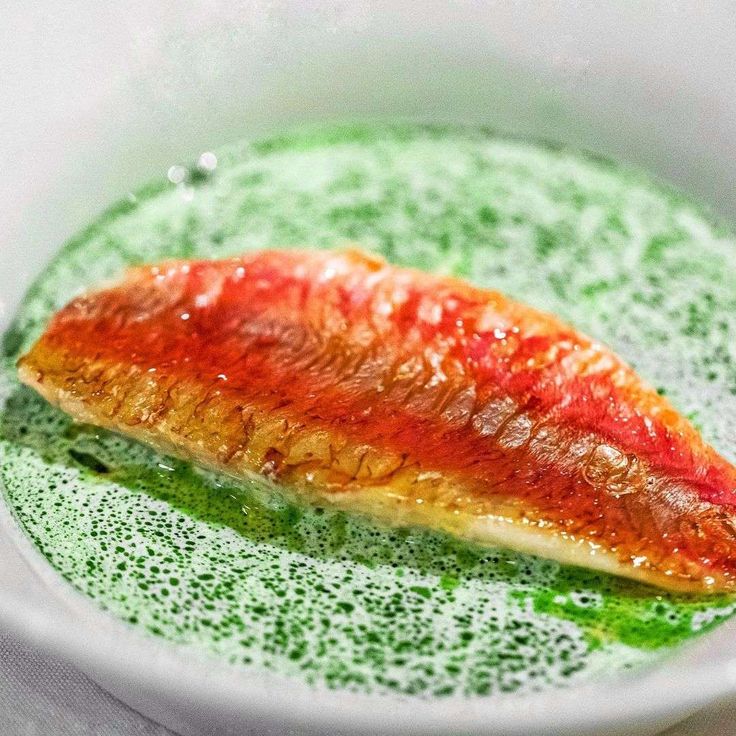 a piece of fish sitting on top of a green substance in a bowl with sauce