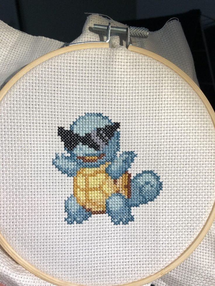 the stitcher is holding up a small cross - stitched blue cat with a yellow ball in it's paws