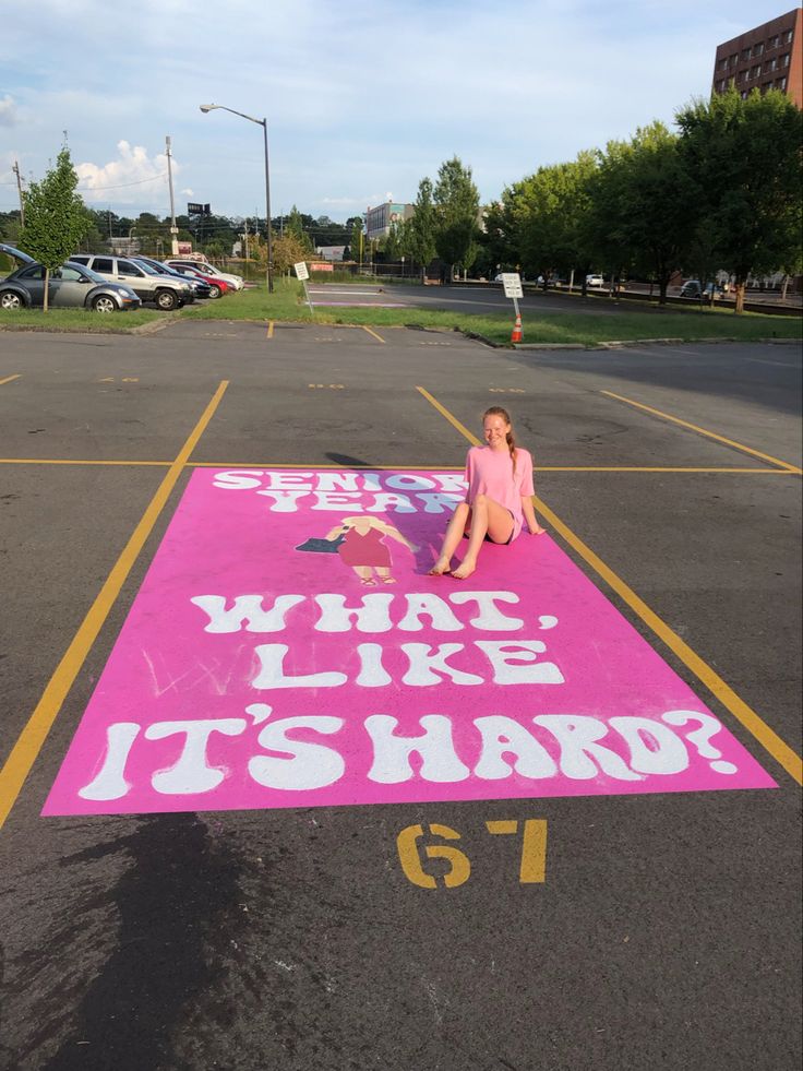 a woman sitting on top of a pink sign in the middle of a parking lot