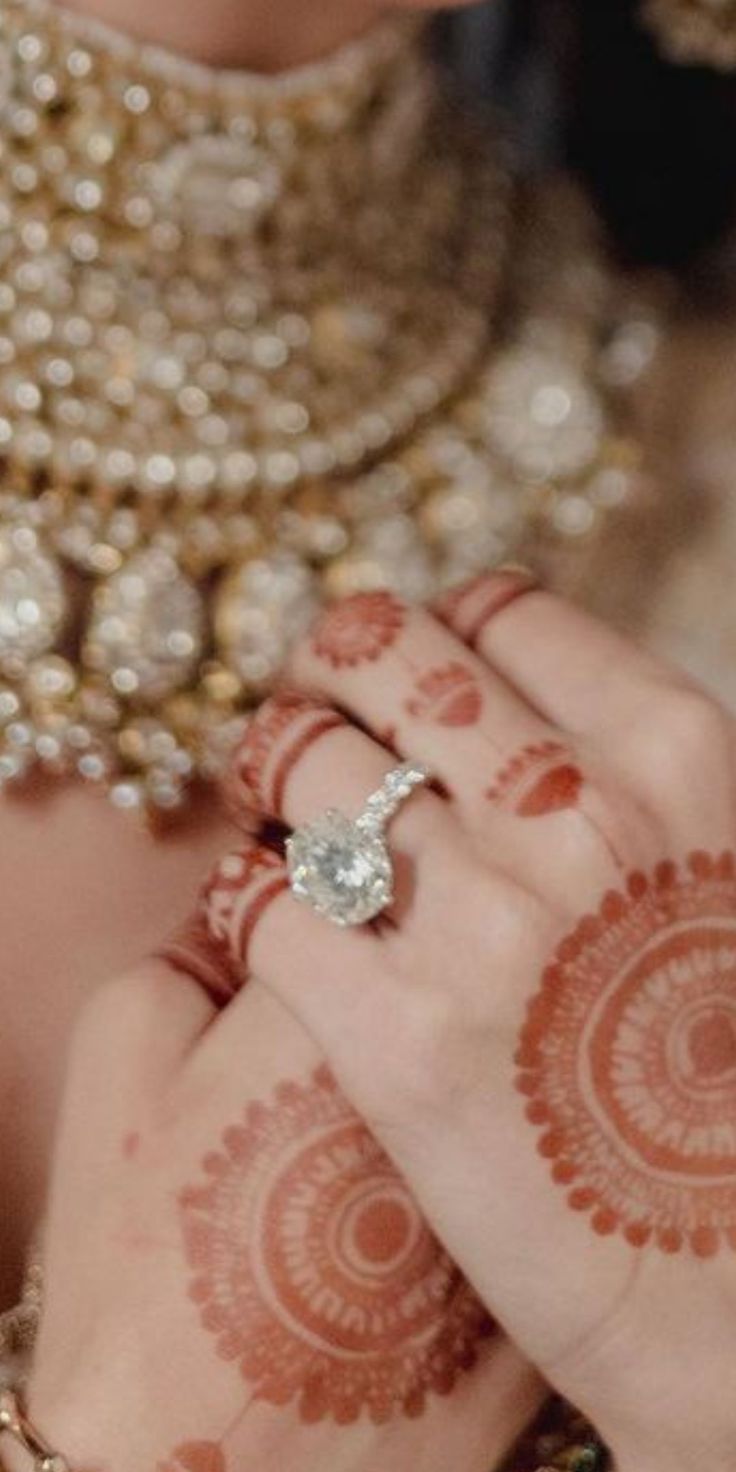 a close up of a person with henna on their hands and holding a ring