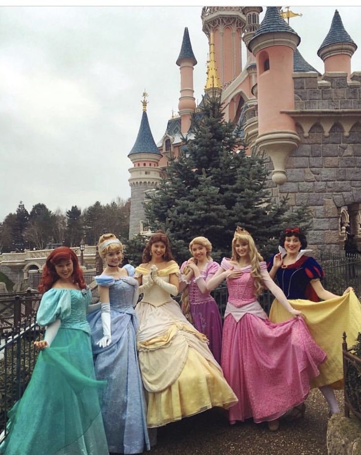 four women dressed in princess dresses posing for a photo with the castle in the background