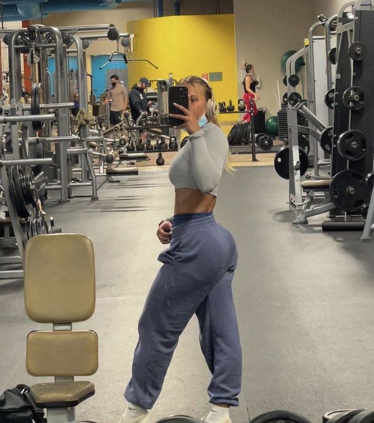 a woman taking a selfie in the gym with her cell phone while wearing sweatpants