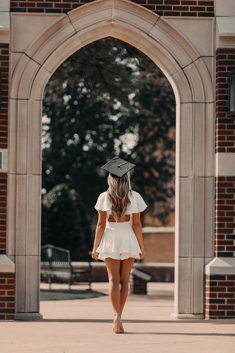 a woman wearing a graduation cap walks through an archway