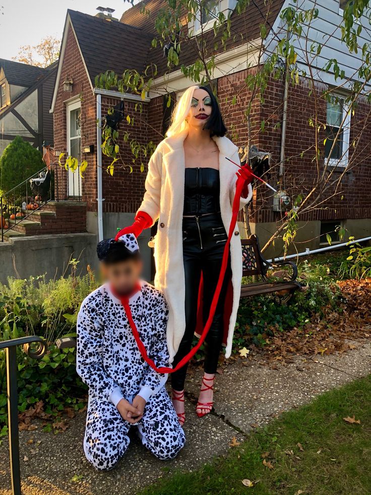 a woman in black and white outfit standing next to a child wearing a red leash