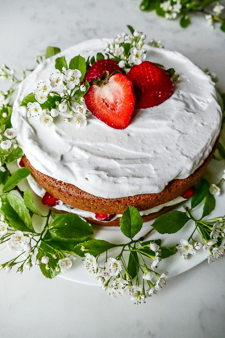 a cake with white frosting and two strawberries on top, surrounded by greenery