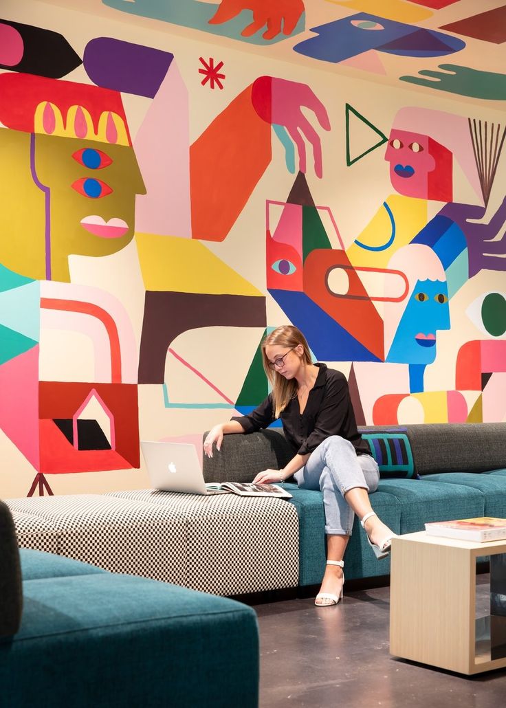 a woman sitting on a couch in front of a colorful wall with abstract shapes and colors