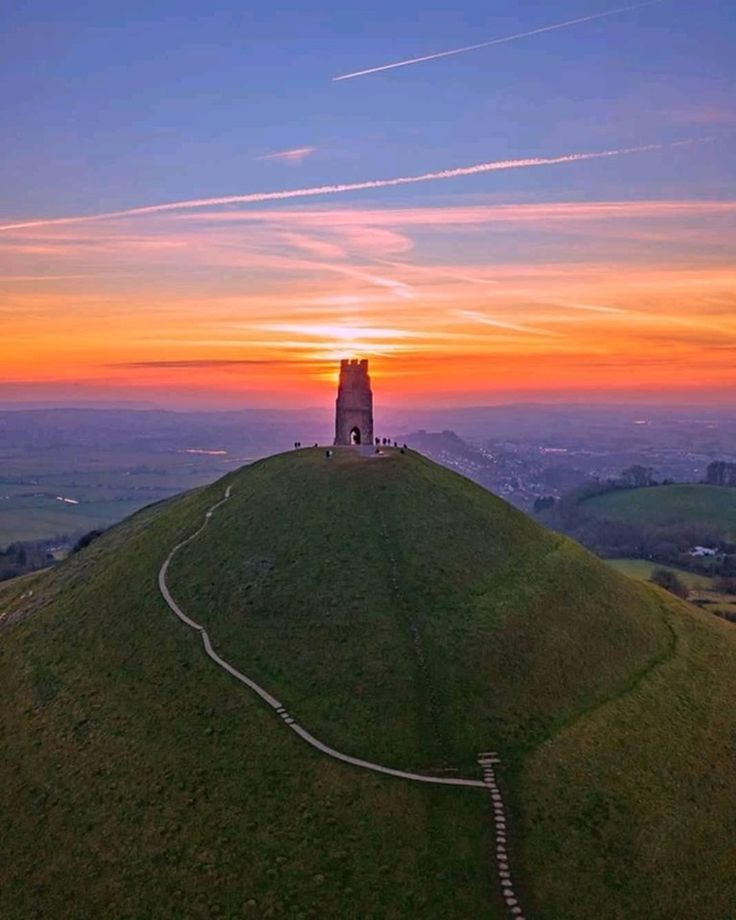 the sun is setting over a grassy hill with a tower on it's top