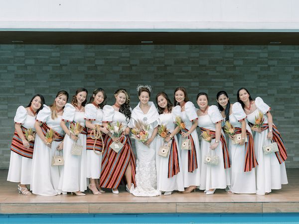 a group of women standing next to each other in front of a swimming pool wearing white dresses