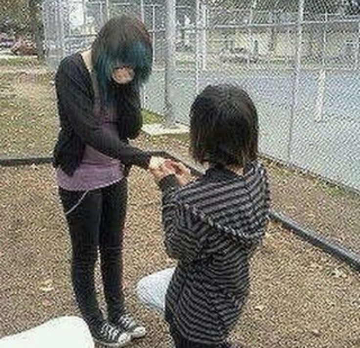 two young children standing next to each other in front of a fenced in area