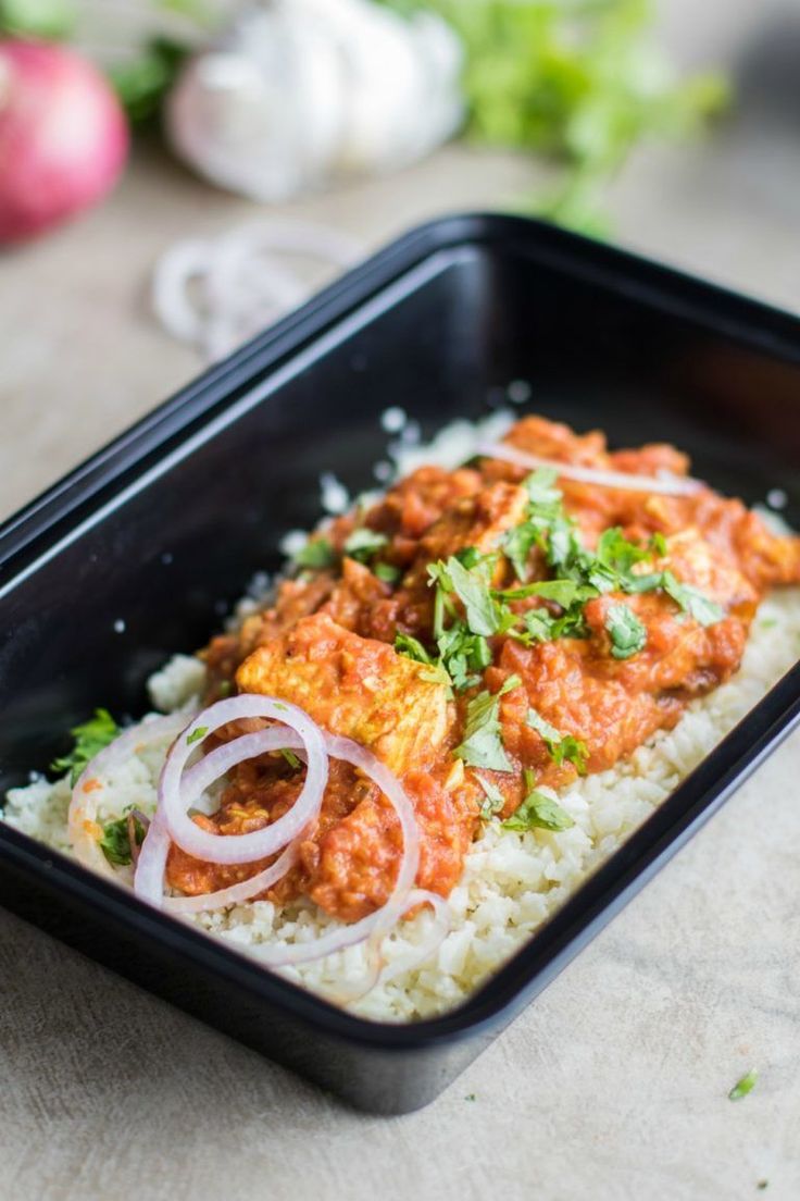 a black container filled with rice covered in sauce and onions on top of a wooden table