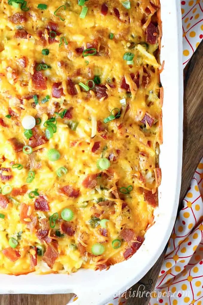 a casserole dish with bacon, cheese and green onions in it on a wooden table