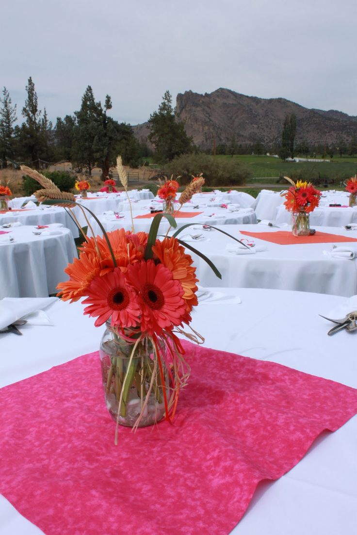 a vase filled with red flowers sitting on top of a table covered in white linens