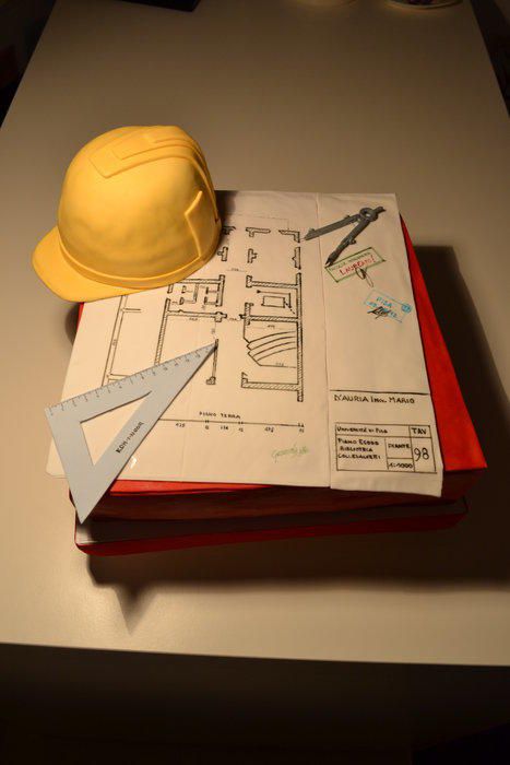 a yellow hard hat sitting on top of an open book next to construction drawings and scissors