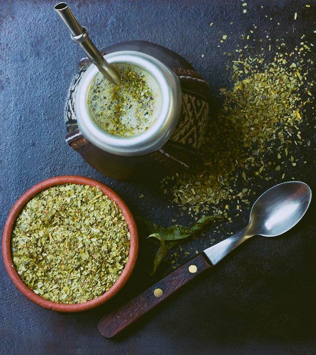 two bowls filled with green tea next to spoons on top of a blue surface