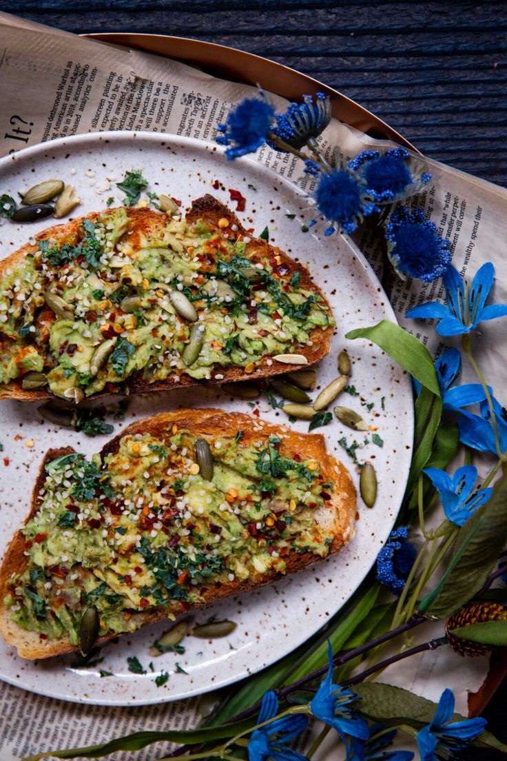 two pieces of bread on a plate with blue flowers and leaves around it next to a newspaper