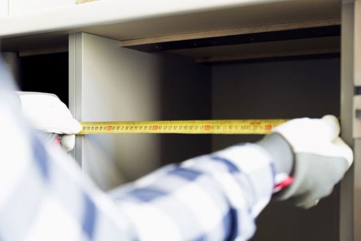 a person measuring the height of a cabinet with a yellow tape on it's edge