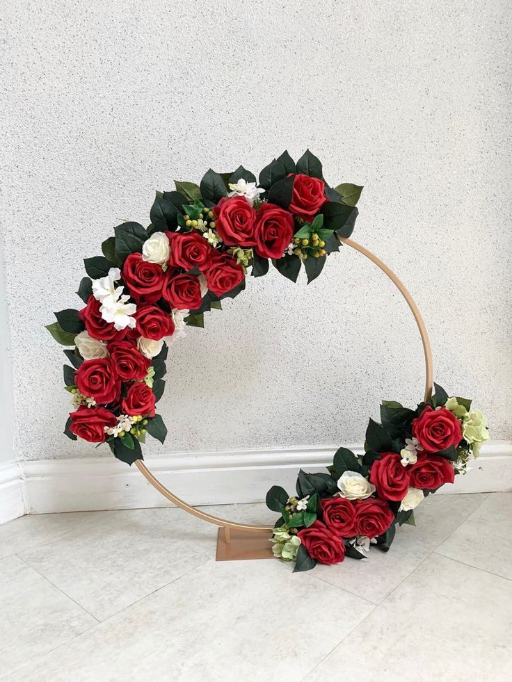 a wreath with red roses and white flowers on the bottom is placed in front of a wall