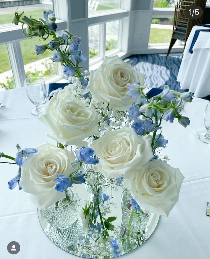 white roses and blue flowers in a glass vase on a table at a wedding reception