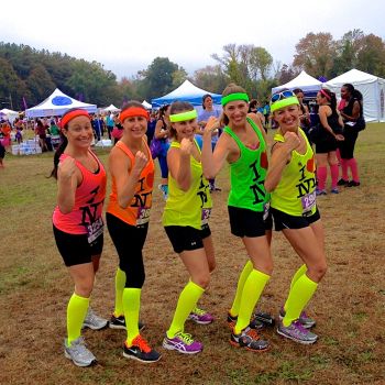 three girls in neon shirts and shorts posing for the camera with their hands up at an outdoor event