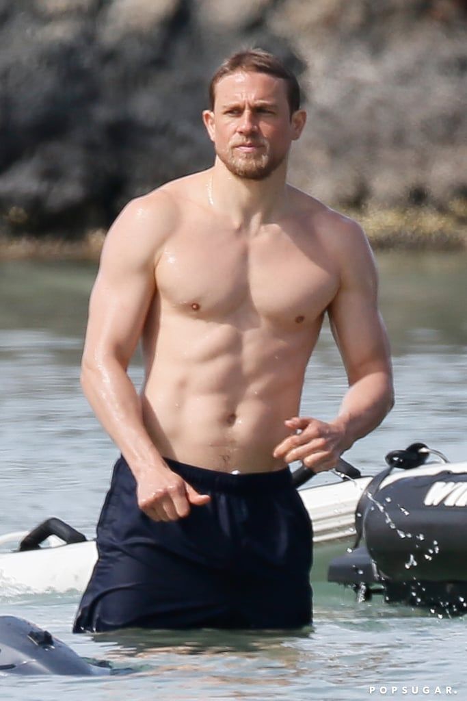 a shirtless man standing in the water next to a boat with his hands on his hips