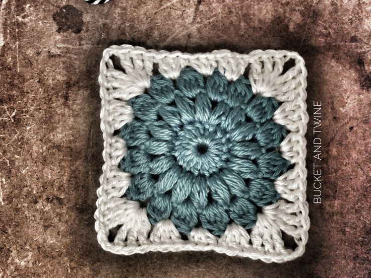 a crocheted square with a blue and white flower on the center is shown